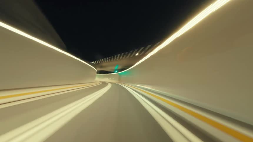 Futuristic point-of-view hyper-lapse of a fast drive on a highway at night, with light trails streaking past and into a brightly lit tunnel