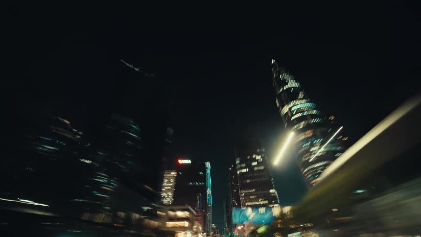 A dynamic hyper-lapse from a car driving through a futuristic city at night, capturing the towering, illuminated skyscrapers