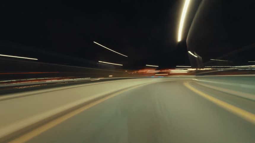 Cinematic point-of-view hyperlapse of a car speeding down an empty highway at night, with city lights streaking past