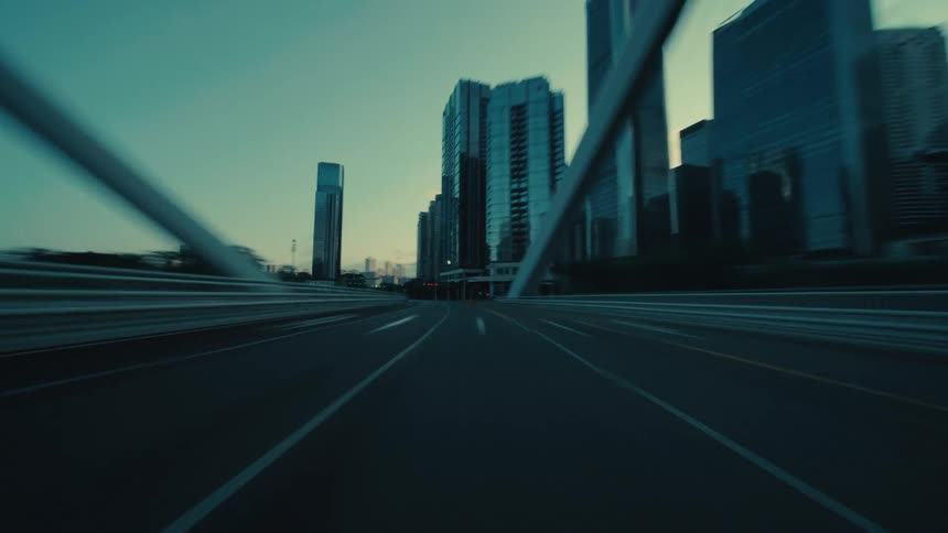 An exhilarating hyperlapse from a low angle speeds through the moody, empty streets of a modern metropolis at twilight