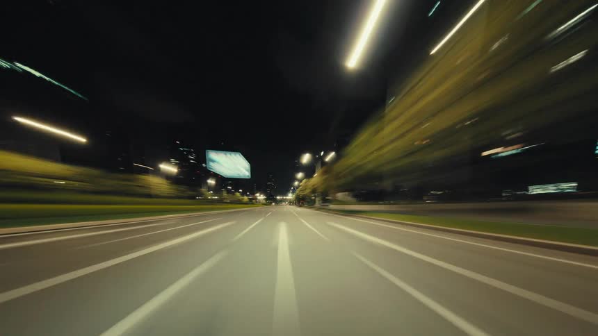 Point-of-view time-lapse shows a car speeding through an empty city underpass and street at night