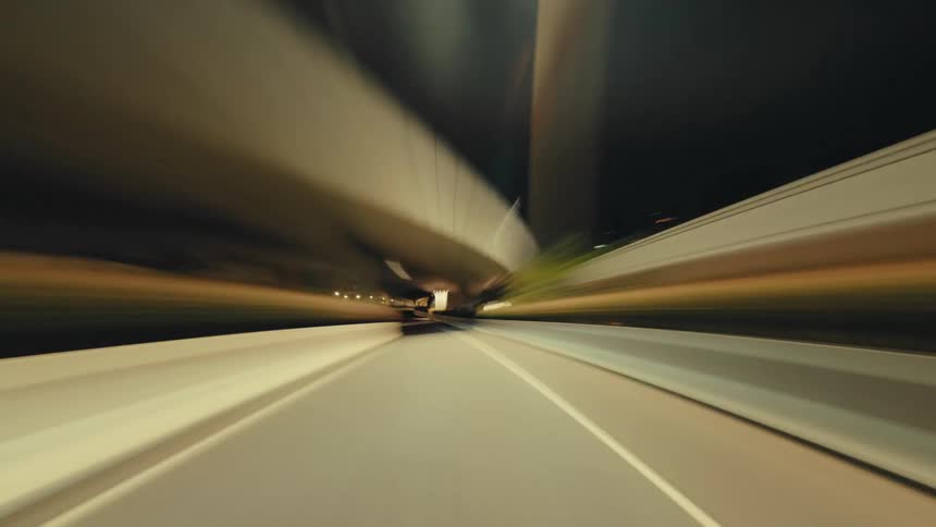 A dynamic hyper-lapse captures a high-speed drive through a city highway at night, with brilliant light trails creating a sense of motion