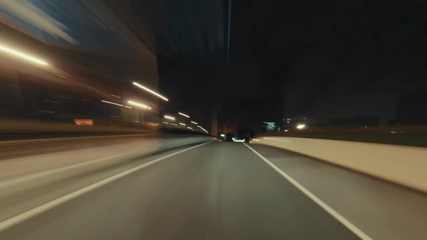 A dynamic first-person point-of-view hyperlapse shows a car speeding along a highway at night, with city lights blurring into long streaks