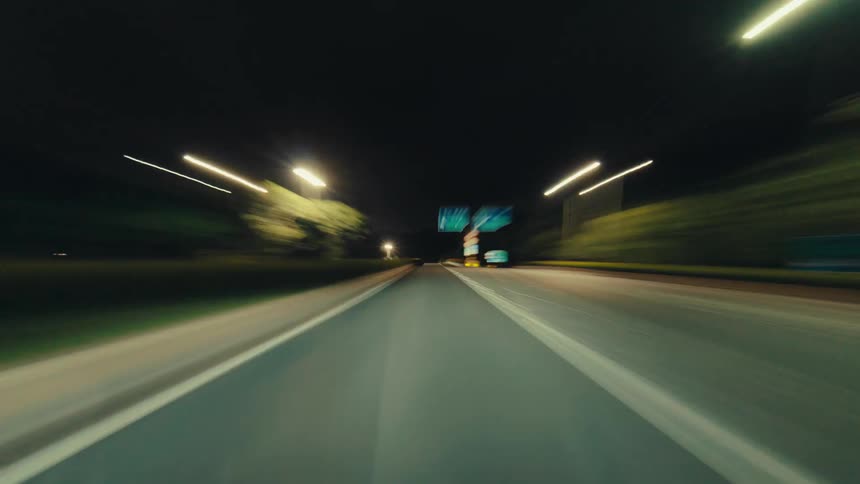 A high-speed hyperlapse from a driver's point of view captures the dizzying motion blur and light trails of a city highway at night