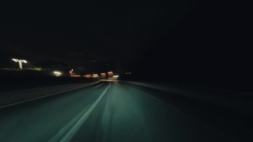 An energetic point-of-view hyperlapse shows a car driving at high speed through a city at night, with streetlights blurring into streaks