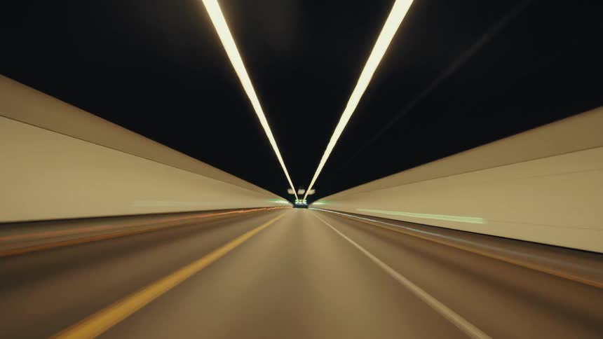 A futuristic hyperlapse from a driver's perspective speeds through an illuminated tunnel and onto the highway at night