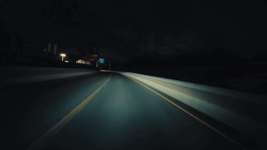 A fast-paced time-lapse from a driver's point of view speeding through an illuminated tunnel and onto a city highway at night