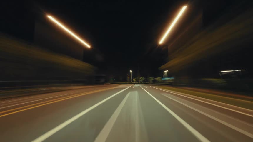 A thrilling hyperlapse of driving down a brightly lit city highway at night, with light trails creating a sense of incredible speed