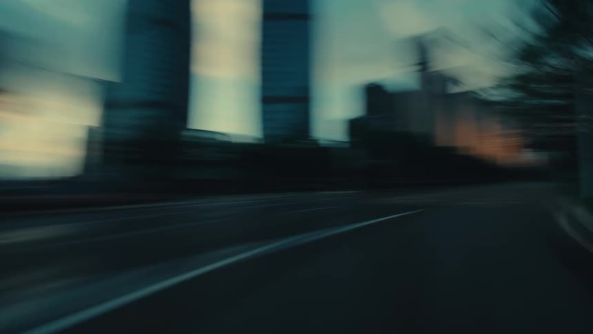 A low-angle hyperlapse perspective speeds down an empty city street at sunrise, with modern skyscrapers blurring past