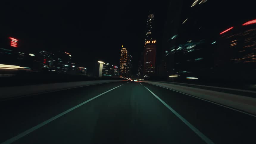 A fast-paced POV hyperlapse of driving through a modern city at night with vibrant light trails
