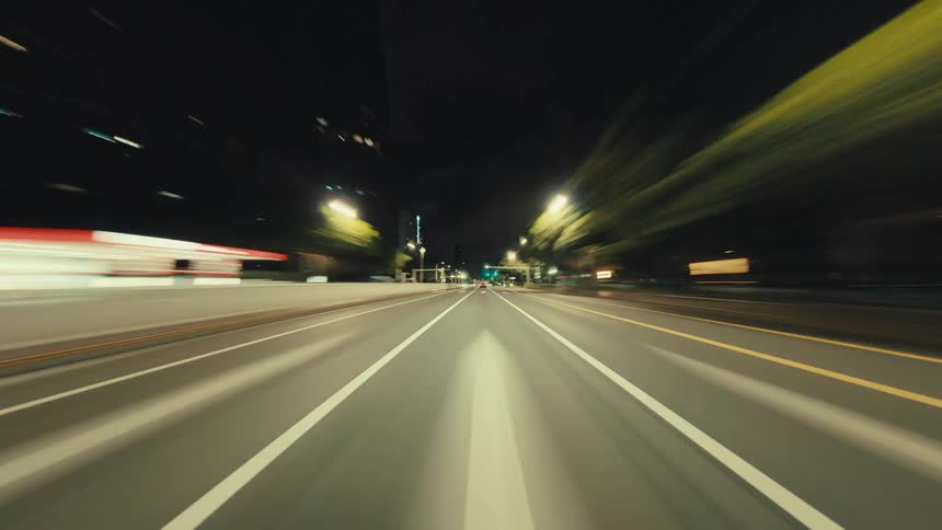 A thrilling POV hyperlapse drive through a modern city at night, with light trails from traffic and streetlights blurring past