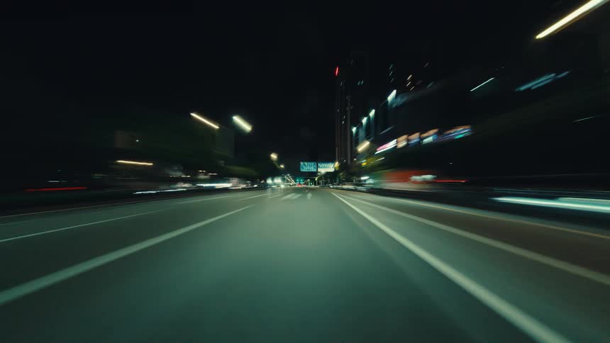 Point-of-view hyperlapse of a fast drive through illuminated city streets at night, creating mesmerizing light trails and a sense of speed
