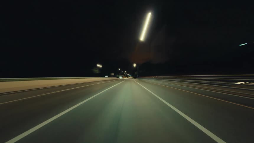 A fast-paced and blurry point-of-view hyperlapse of a car driving on a highway at night