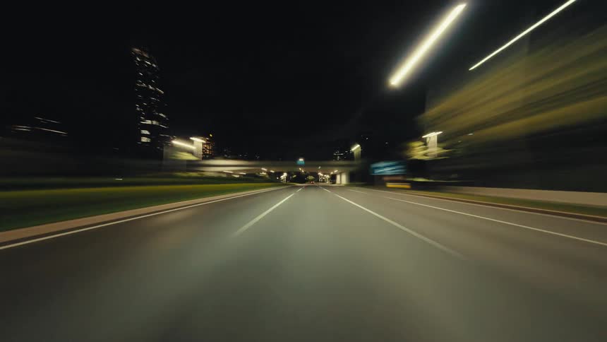 A thrilling first-person point-of-view hyperlapse of driving at high speed through a modern city's illuminated streets and tunnels at night