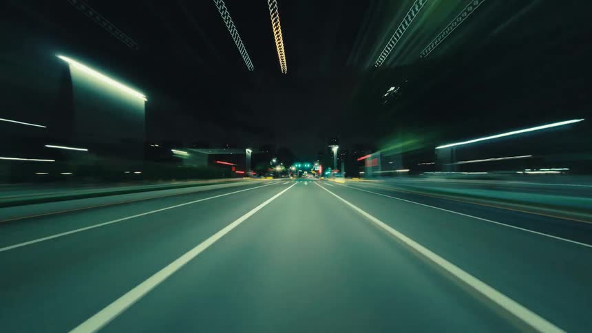 A surreal hyper-lapse captures a high-speed point-of-view drive through a city at night, with motion-blurred lights creating vibrant streaks of color