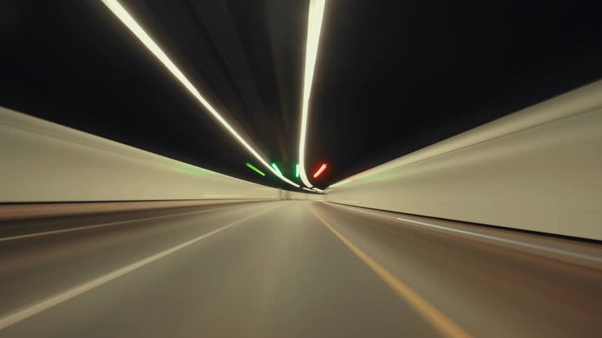 An immersive, point-of-view time-lapse of a vehicle speeding through a brightly lit highway tunnel, with lights creating abstract streaks