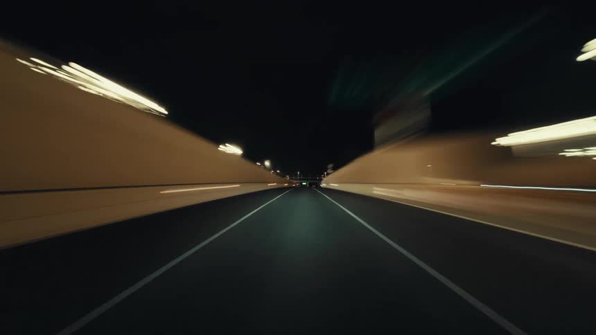 A futuristic POV hyperlapse of a car driving at high speed through an illuminated tunnel and onto a dark highway at night