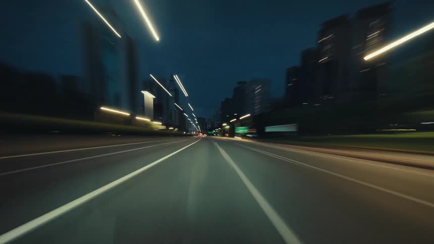 An energetic POV hyperlapse shows a speedy journey through a city's highway at night, with streaking light trails from buildings and streetlights
