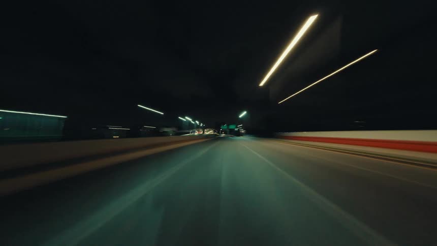 A first-person point-of-view hyper-lapse of driving through city streets and into an illuminated tunnel at night, creating streaks of light