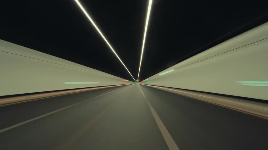 Point-of-view time-lapse captures a high-speed journey through a brightly lit, modern highway tunnel at night, creating streaks of light