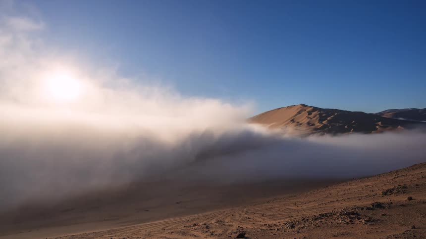Breathtaking timelapse of a sunrise over desert sand dunes, with a river of fog flowing through the valley below