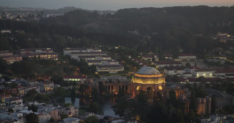 A majestic high-angle view of the illuminated Palace of Fine Arts in San Francisco at dusk, nestled among the city's hills