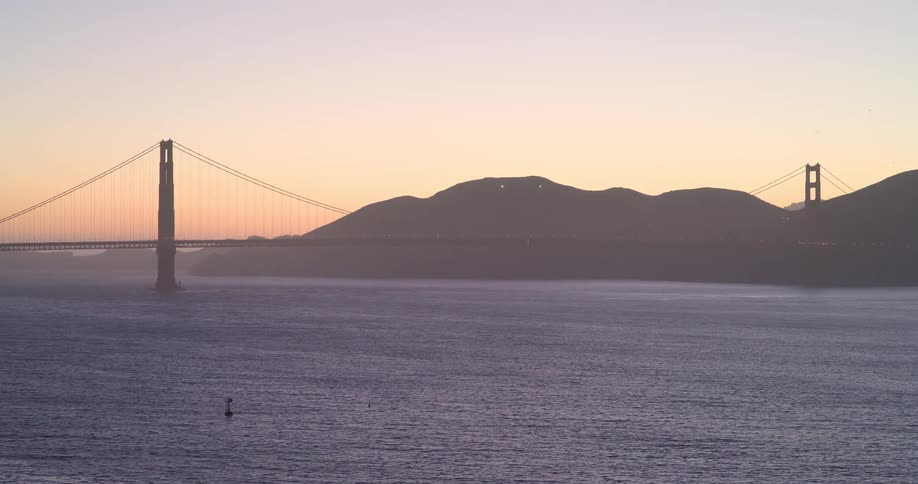 The iconic Golden Gate Bridge is silhouetted by a hazy sunrise over the San Francisco Bay