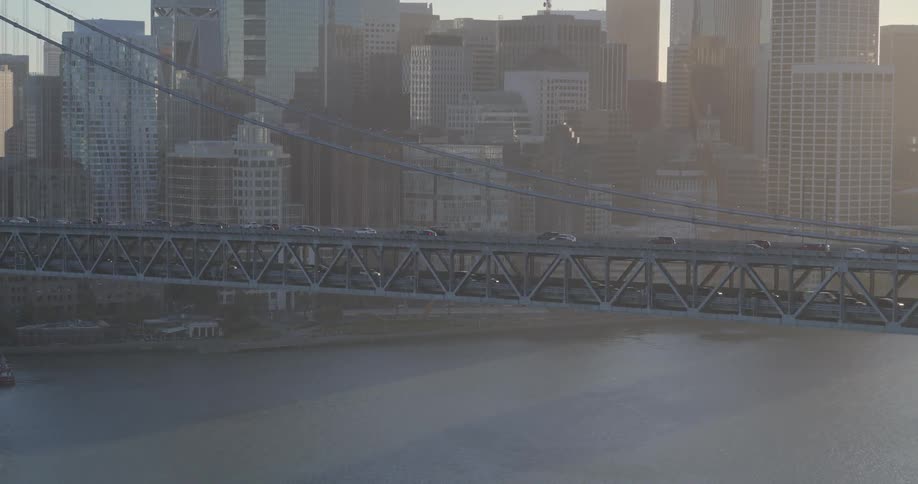 An aerial view of traffic crossing the San Francisco Bay Bridge with the hazy city skyline in the background during a golden sunset
