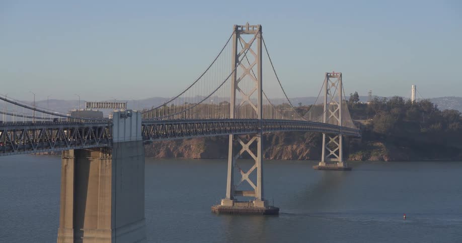 A wide, slow zoom-out shot captures the majestic San Francisco-Oakland Bay Bridge over the calm bay waters on a clear sunny day