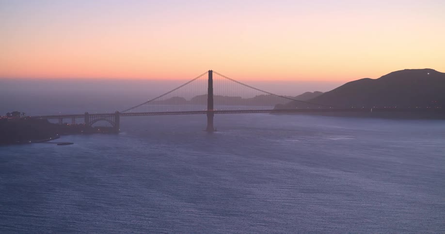 The iconic Golden Gate Bridge is silhouetted against a beautiful hazy sunset over the San Francisco Bay