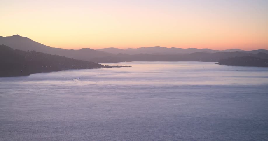 A tranquil wide shot of a vast bay during a beautiful sunset as a boat cruises through the calm waters
