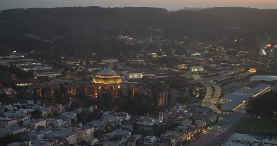 A stunning aerial view of the illuminated Palace of Fine Arts in San Francisco at twilight, with city lights and traffic below