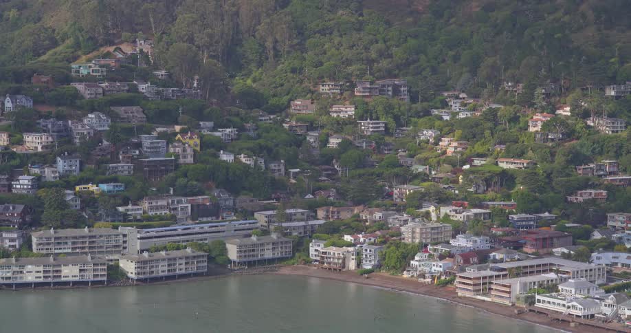 A scenic view of a train passing through the coastal town of Sausalito, California, nestled in the green hillsides along the bay