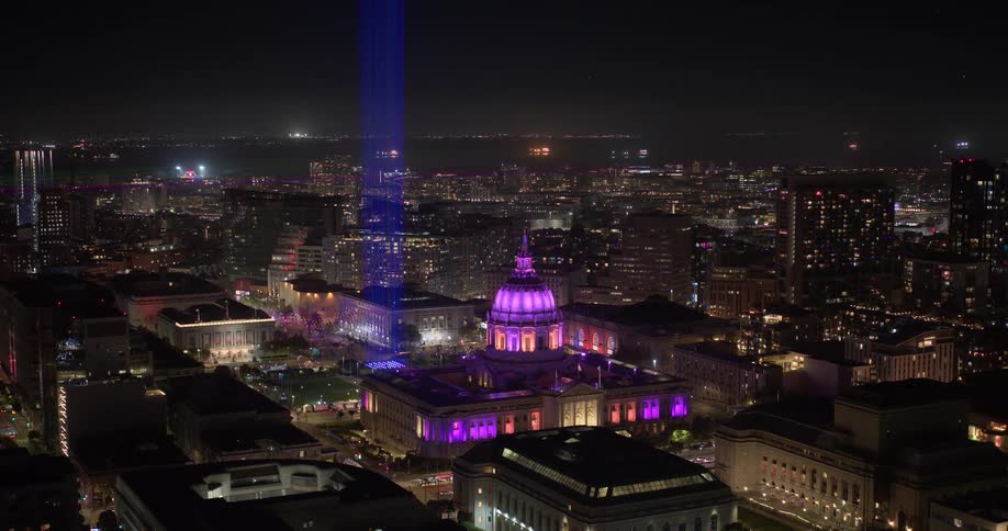 A colorful timelapse of San Francisco City Hall illuminated in purple with a laser light show beaming into the night sky over the city