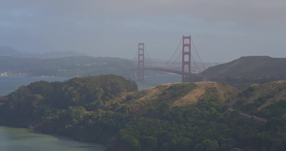 An aerial view of the Golden Gate Bridge partially obscured by thick fog, with the lush Marin Headlands in the foreground