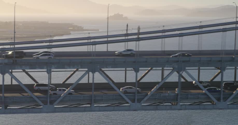 An aerial view shows cars and trucks driving along the upper and lower decks of the San Francisco Bay Bridge during a hazy golden hour
