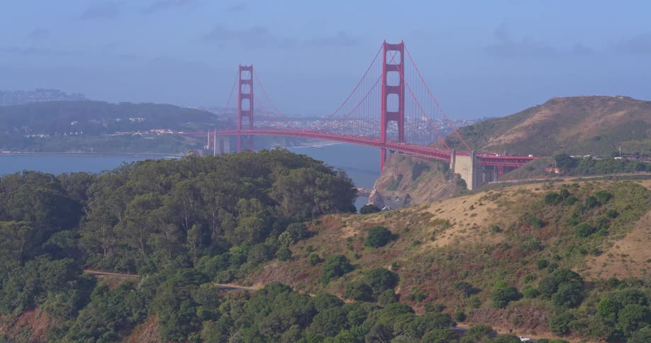 A slow aerial push-in shot reveals the iconic Golden Gate Bridge from the Marin Headlands on a clear, sunny day