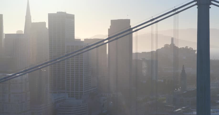 An ethereal aerial shot pulls back to reveal the iconic San Francisco skyline, including the Transamerica Pyramid and Coit Tower, shrouded in a warm, hazy morning light