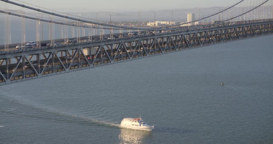 An aerial shot captures rush hour traffic on the San Francisco Bay Bridge as a boat sails on the water below