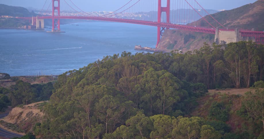 An aerial view pulls back from a forested hillside to reveal the iconic Golden Gate Bridge in San Francisco