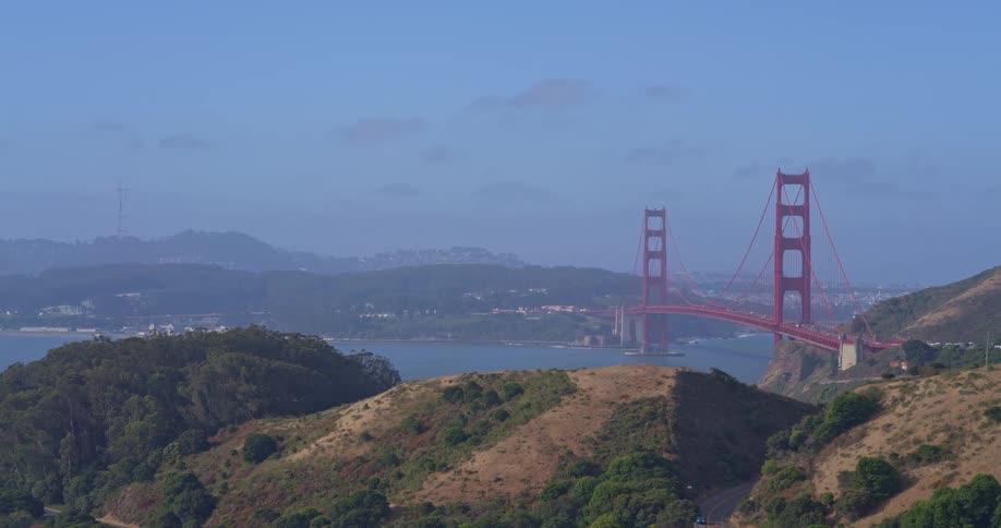Aerial view pans left across the Marin Headlands, revealing the iconic Golden Gate Bridge and San Francisco Bay on a sunny day