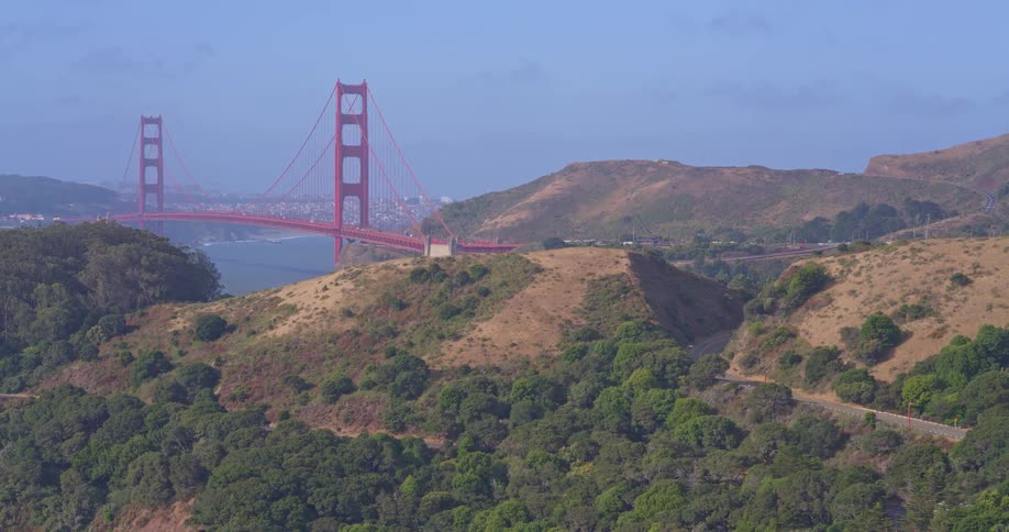 An aerial view of the rolling hills of the Marin Headlands with the iconic Golden Gate Bridge in the background on a clear, sunny day