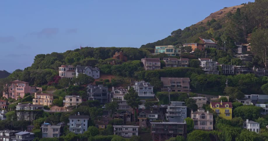 An aerial view rises over the waterfront homes and lush green hills of Sausalito to reveal the iconic Golden Gate Bridge in the distance