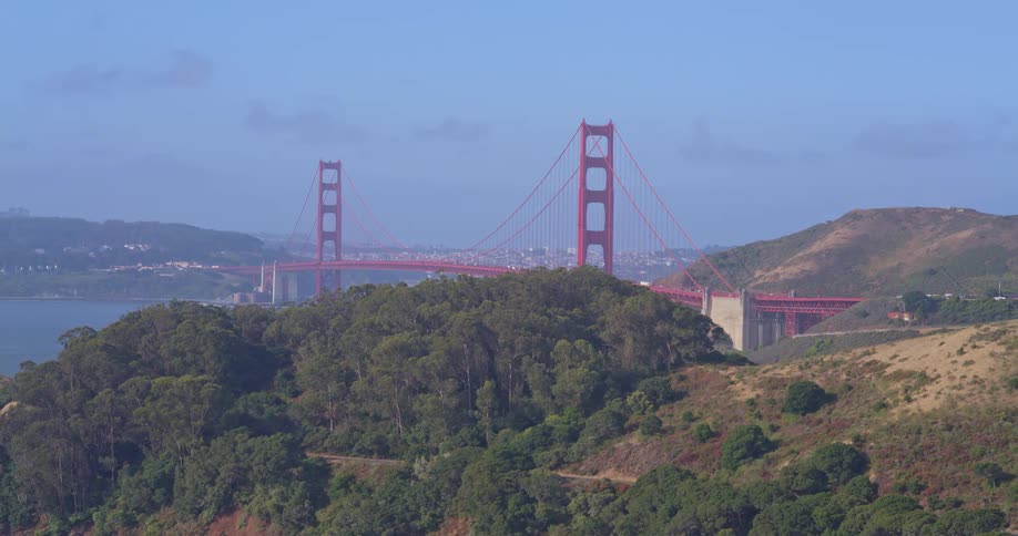 A slow aerial reveal of the iconic Golden Gate Bridge spanning the San Francisco Bay, with the Marin Headlands in the foreground