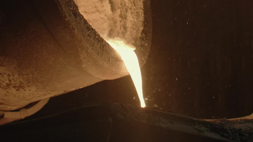Molten metal is poured from a large crucible into a mold at an industrial foundry
