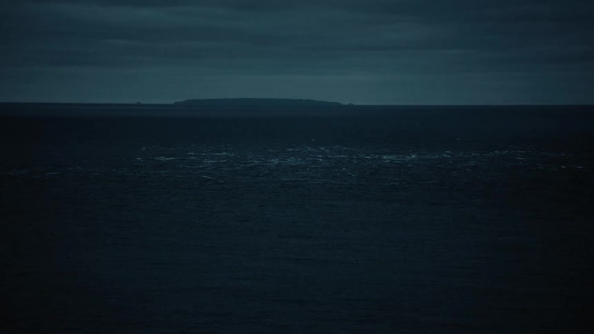 The mysterious silhouette of a distant island looms over a dark, churning ocean under a cloudy night sky