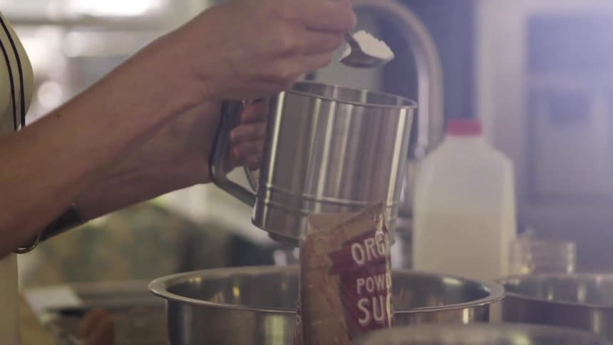 Woman scoops powdered sugar into a sifter