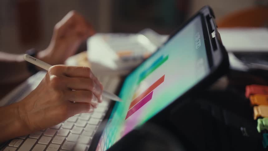 A person uses a stylus to analyze a colorful bar graph on a tablet screen while working from home