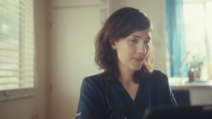 Slow push-in shot of a female doctor in scrubs working on a tablet in a sunny room