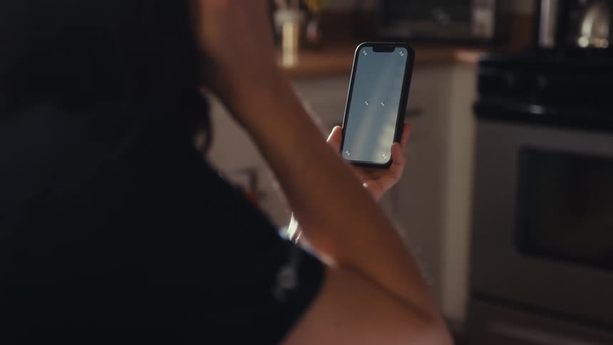 Over-the-shoulder shot of a person holding a smartphone with a tracking screen in a sunlit kitchen